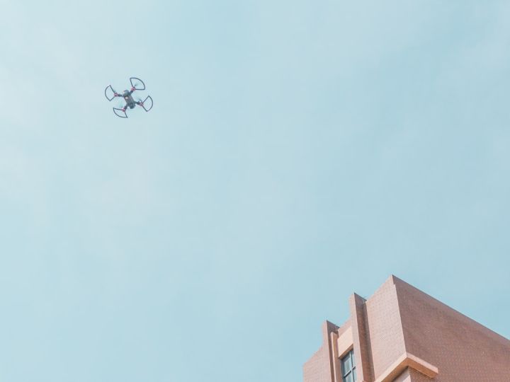 Drone - white quadcopter drone fly near brown concrete building