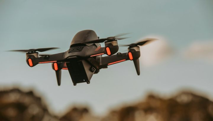 FPV - gray and orange drone flying in mid air during daytime