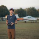 Remote Control Planes - a young man standing in a field holding a camera