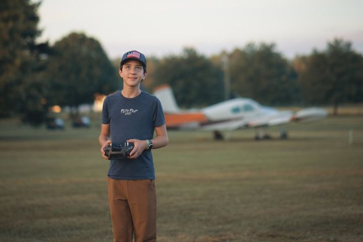 Remote Control Planes - a young man standing in a field holding a camera