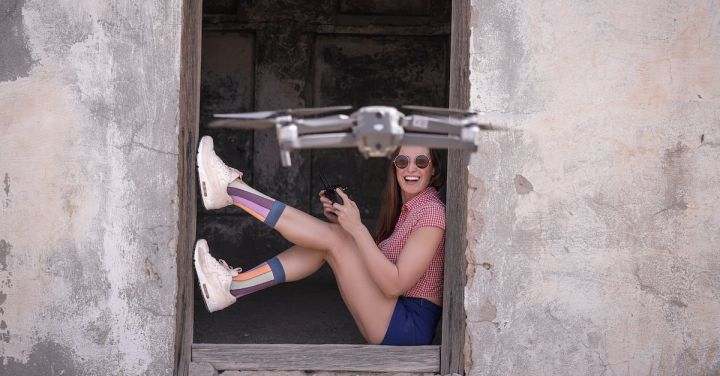 Remote Control Planes - Side view full body excited female in casual wear sitting at remaining hut entrance and operating modern drone