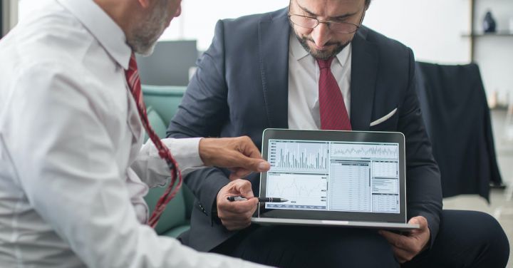 Economic Outlook - Men in Suits Discussing Graphs on Laptop Screen